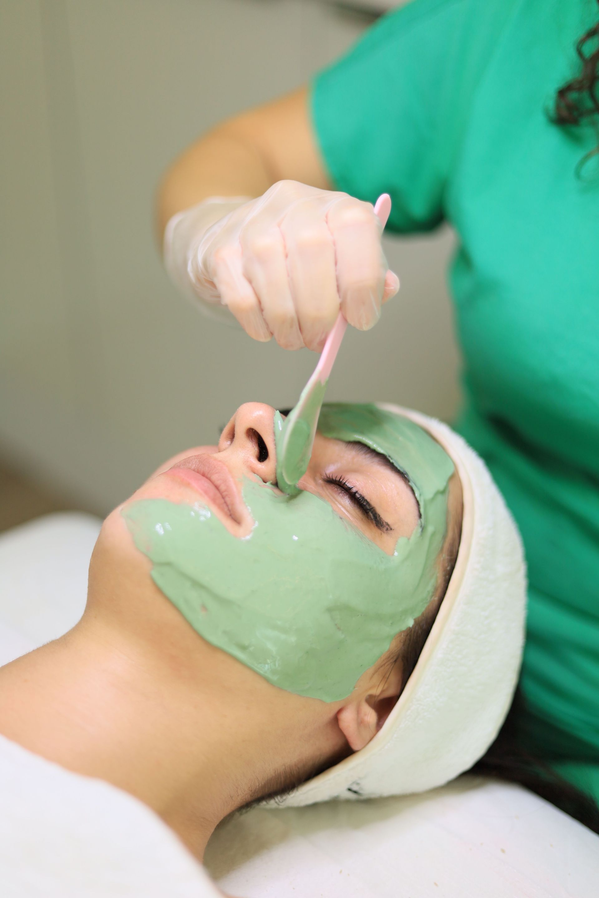 A woman enjoys a rejuvenating green clay mask facial treatment at a spa.